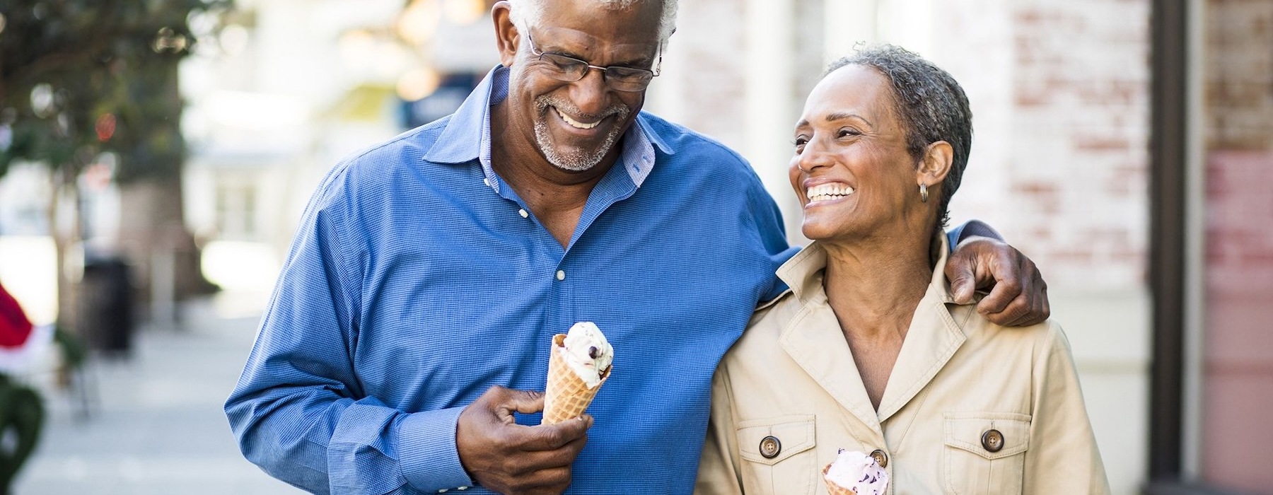 older couple walks down city sidewalk while holding ice cream cones